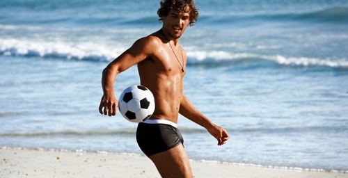 парень в плавках на пляже с футбольным мячом