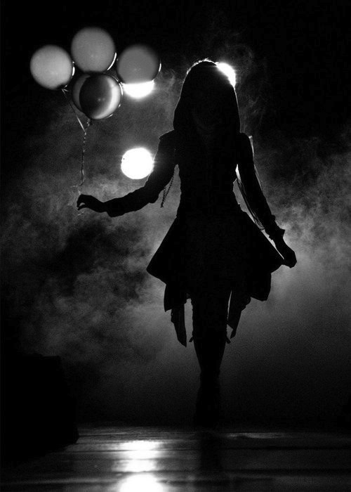 силуэт девушки с воздушными шарами ночью в темноте при свете прожекторов