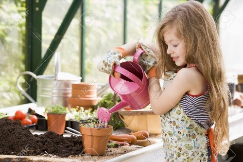 девочка поливает вазоны из лейки в цветочной оранжерее