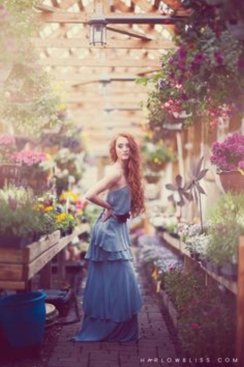 девушка в длинном синем платье среди вазонов цветов в оранжерее