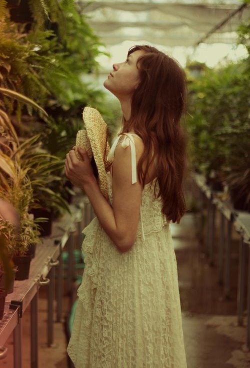 девушка любуется красотой природы в оранжерее держа в руках соломеную шляпку