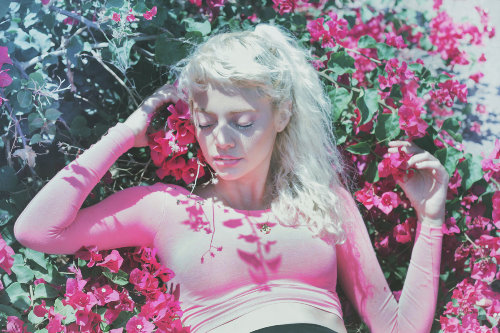 блондинка с бледными ресницами лежит в кустах розовых цветов