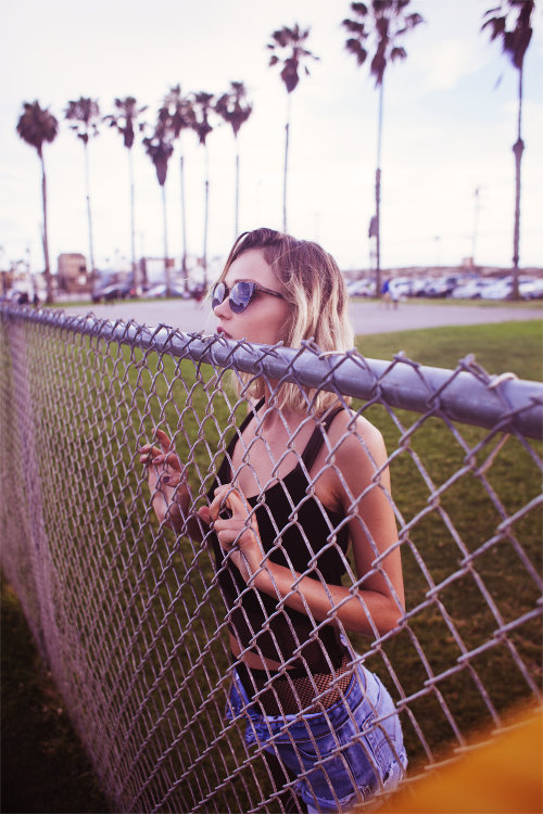 блондинка в солнцезащитных очках выглядывает через забор