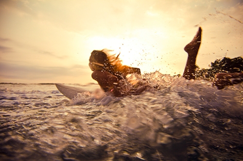 девушка лежит на животе на доске серфинг по волнам на закате