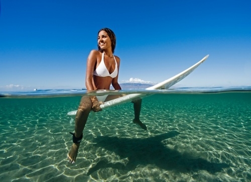 девушка в белом купальнике сидит верхом на доске для серфинга