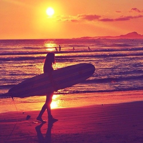 девушка сёрфингистка на закате в лучах солнца на пляже силуэт