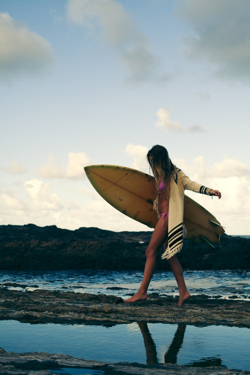 девушка в розовом купальнике где не видно лица с доской для серфинга на каменном пляже