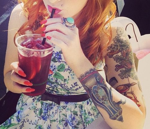 девушка с татуировками пьет через соломинку напиток со льдом