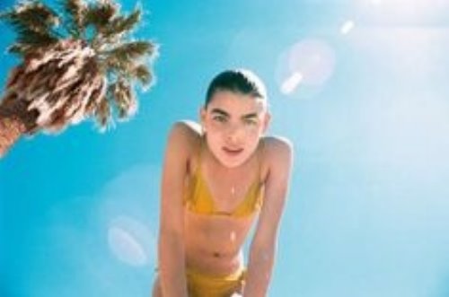 девушка в желтом купальнике наклонилась на пляже с пальмой