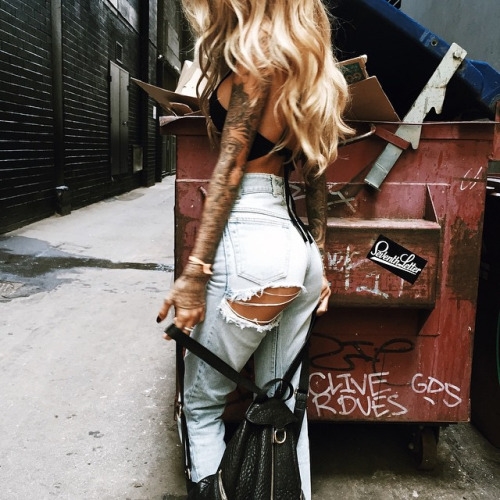 блондинка с татуировками со спины в рваных джинсах в переулке 