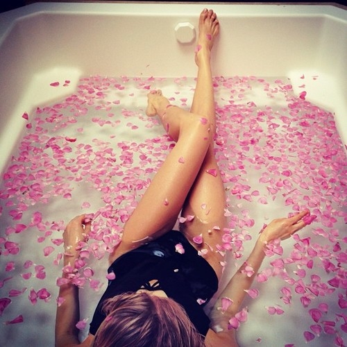 девушка в ванной с розовыми лепестками роз в черном купальнике на спине