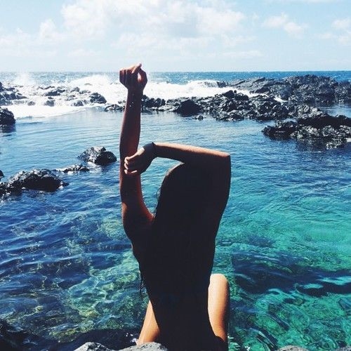 девушка сидит в воде на море подняв руки вверх