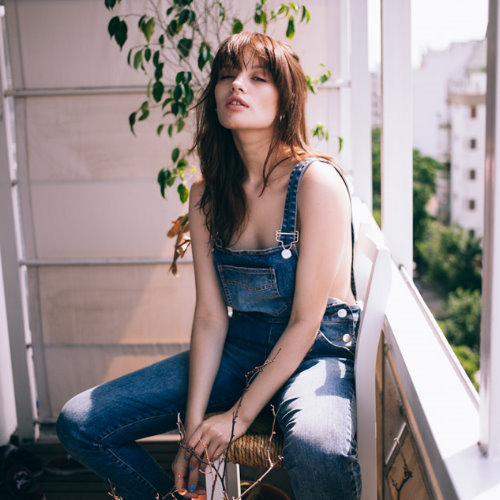 девушка в джинсовом комбинезоне сидит на балконе под солнцем
