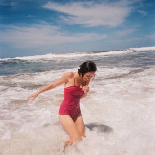 девушка в розовом слитном купальнике смеется ловя волны