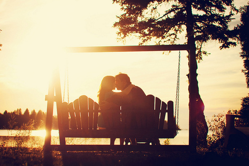 влюбленные качаются на качели-скамейке целуясь в лучах солнца не видно лиц