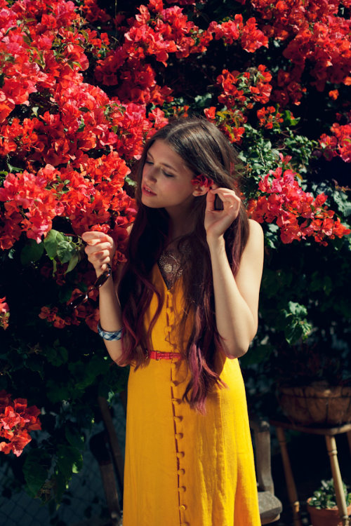 девушка в желтом платье с гладкими волосами прикрепляет красный цветок за ухо