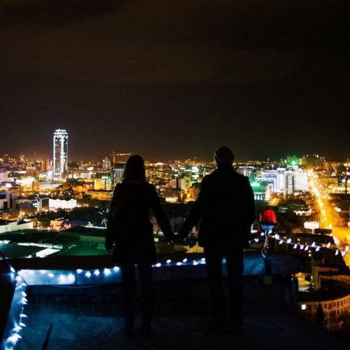влюбленные на крыше украшенной гирляндой смотрят на ночной город