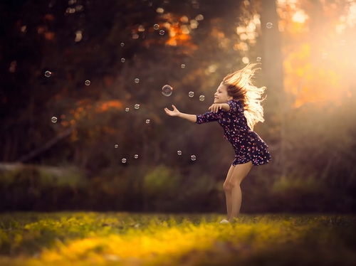 девочка в солнечных лучах играет с мыльными пузырями