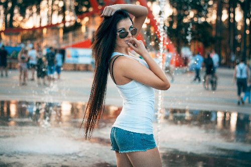 девушка с длинными волосами в коротких джинсовых шортах позирует у фонтана