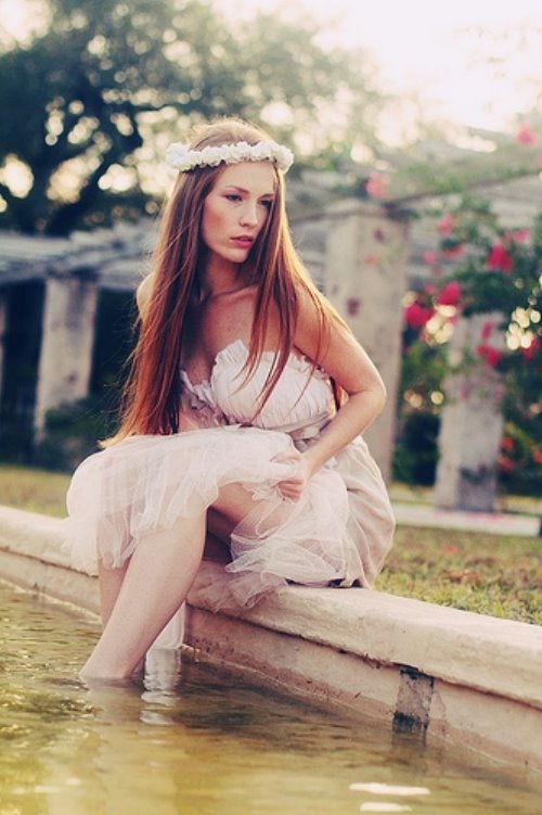девушка в красивом платье в венке сидит на краю фонтана