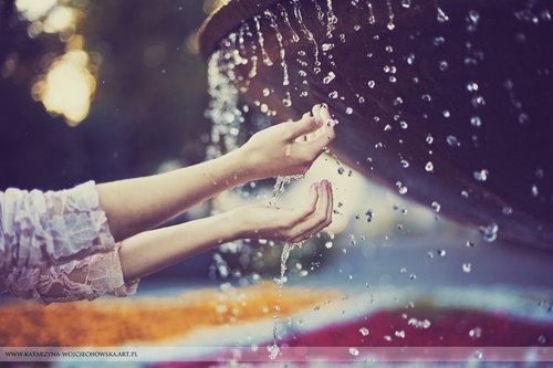 девушка протягивает руки к каплям воды в фонтане