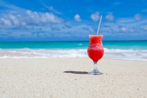 бокал клубничного коктейля стоит в песке у морской воды