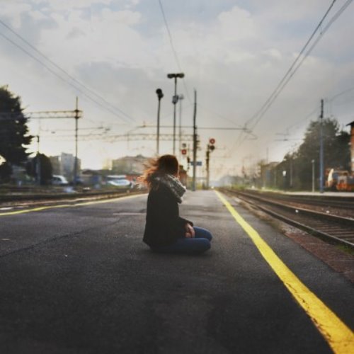 девушка сидит на асфальте на перроне в ожидании поезда