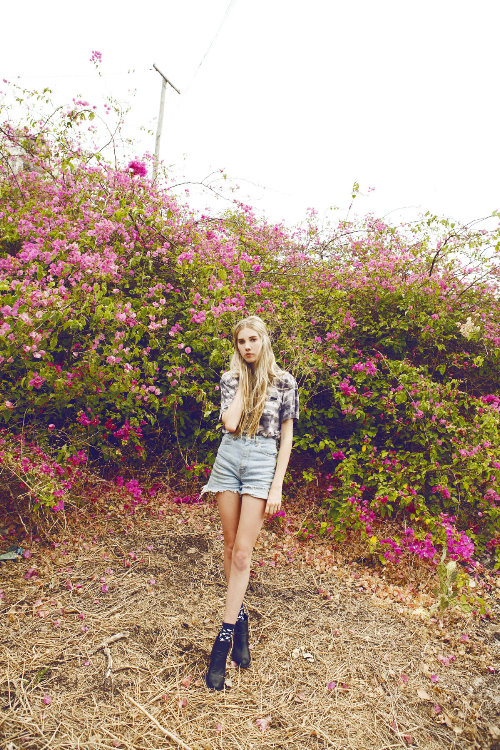 девушка с длинными ногами стоит возле цветущих кустов