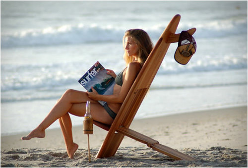 серфингистка сидит на шезлонге на пляже читая журнал
