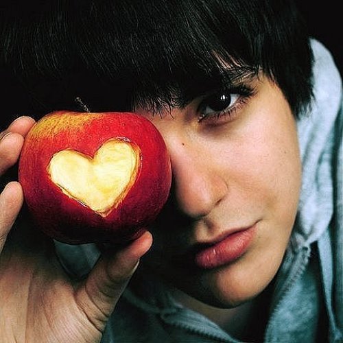 брюнет с карими глазами держит яблоко с вырезанным сердечком