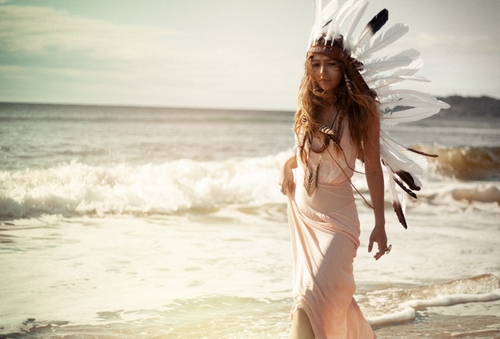 девушка с перьями на голове идет по побережью моря