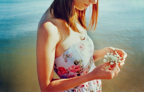 девушка в сарафане на пляже с цветами в руках