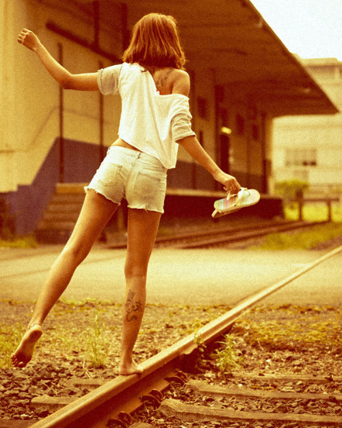 девушка стоит на одной ноге на рельсах