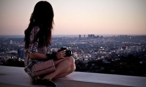 брюнетка с фотоаппаратом и клатчем смотрит панораму вечернего города