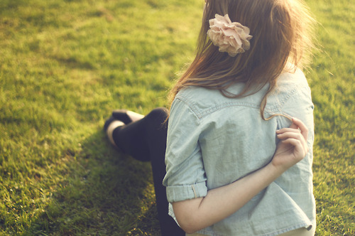 Шатенка сидит на траве задом с цветком в волосах