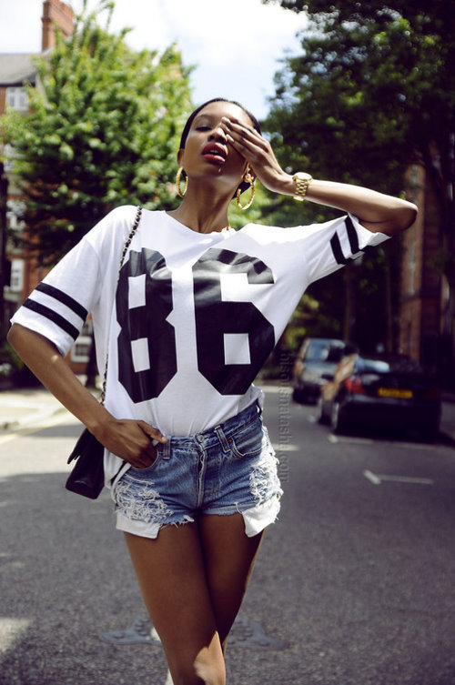 темнокожая девушка с золотыми аксессуарами в коротких джинсовых шортах и белой футболке 86 на улице города летом