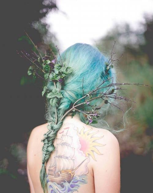Татуировка корабля на спине у девушки с синими волосами, в которые вплетены ветки с листьями.