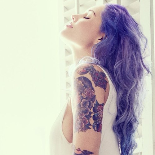 Девушка с фиолетовыми волосами в белой майке, на руке большая цветная татуировка.