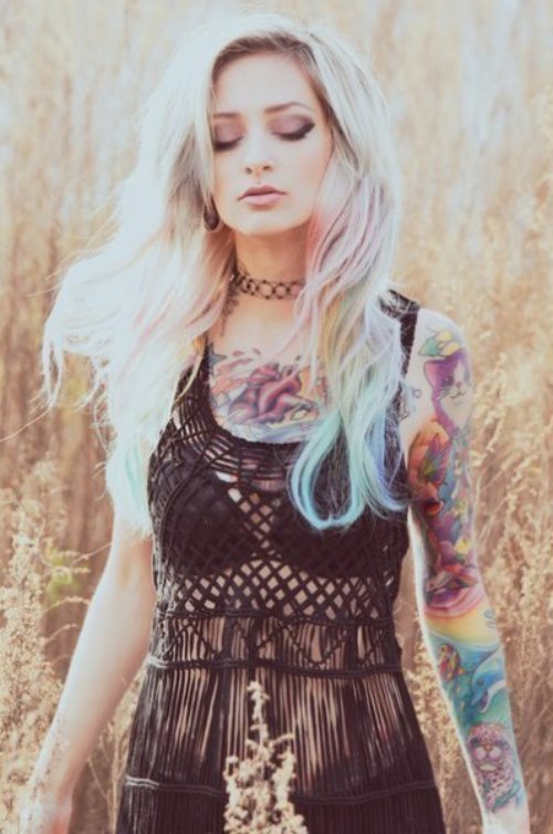 Девушка с разноцветными татуировками и волосами в поле с прозрачной черной майке.