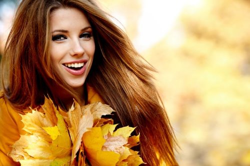 красивая девушка с лучезарной улыбкой прижала к себе букет кленовых листьев