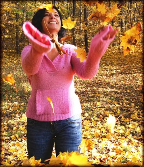 женщина в розовом свитере бросает к небу желтые листья в лесу