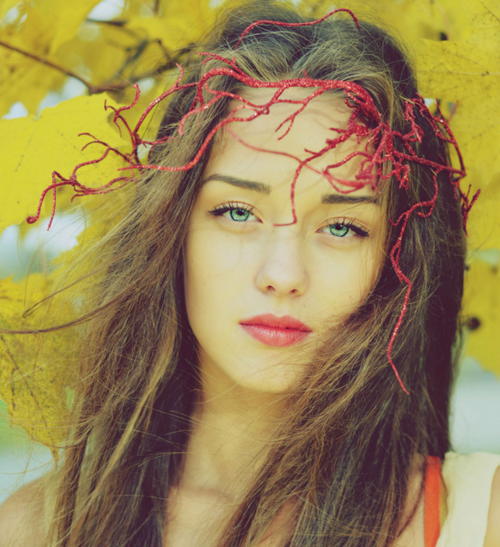 пронзительный взгляд голубых глаз с красным декором ветки в волосах на фоне осенних листьев желтого цвета