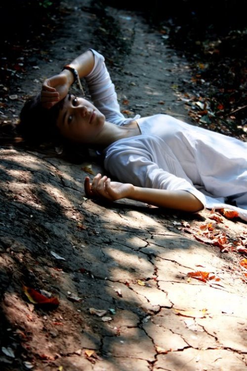Девушка в белой одежде лежит на растрескавшейся земле осенью.