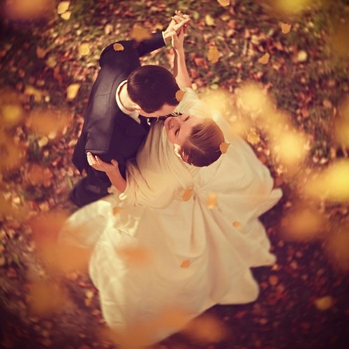 Жених и невеста кружатся в танце среди осеннего листопада. Невеста улыбается. Вид сверху.