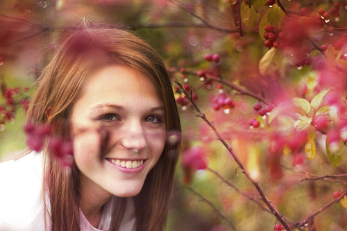 Девушка шатенка мило улыбается среди красных ягод покрытых росой осенью.