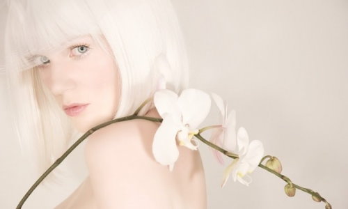 блондинка с каре под белой вуалью держит белую орхидею на голом плече