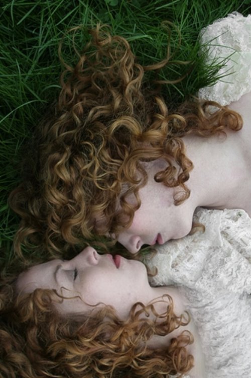 Две девушки с локонами лежат друг к другу носами