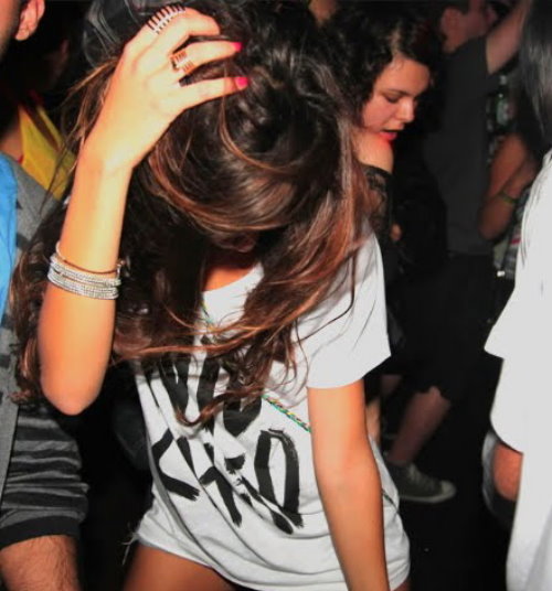 девушка с коричневыми волосами и кольцами пружинами танцует в клубе в белой футболке