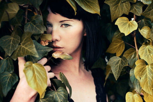 Черноволосая девушка прячется в листьях, портрет