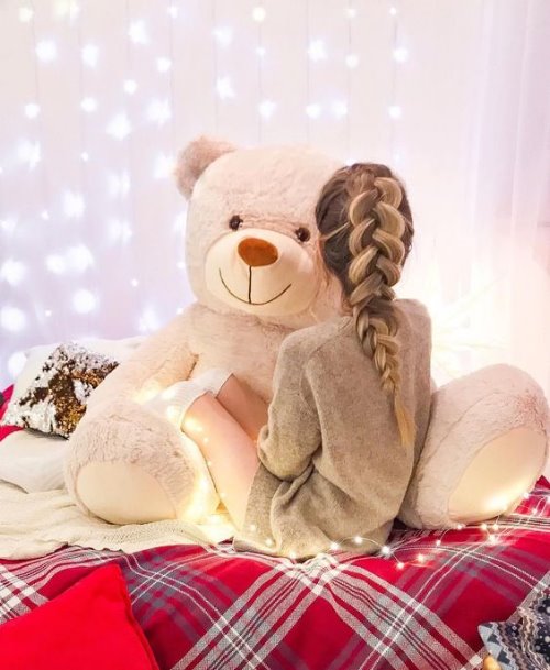 Девушка с большой косой в свитере и гетрах обнимает медведя не видно лица на кровати